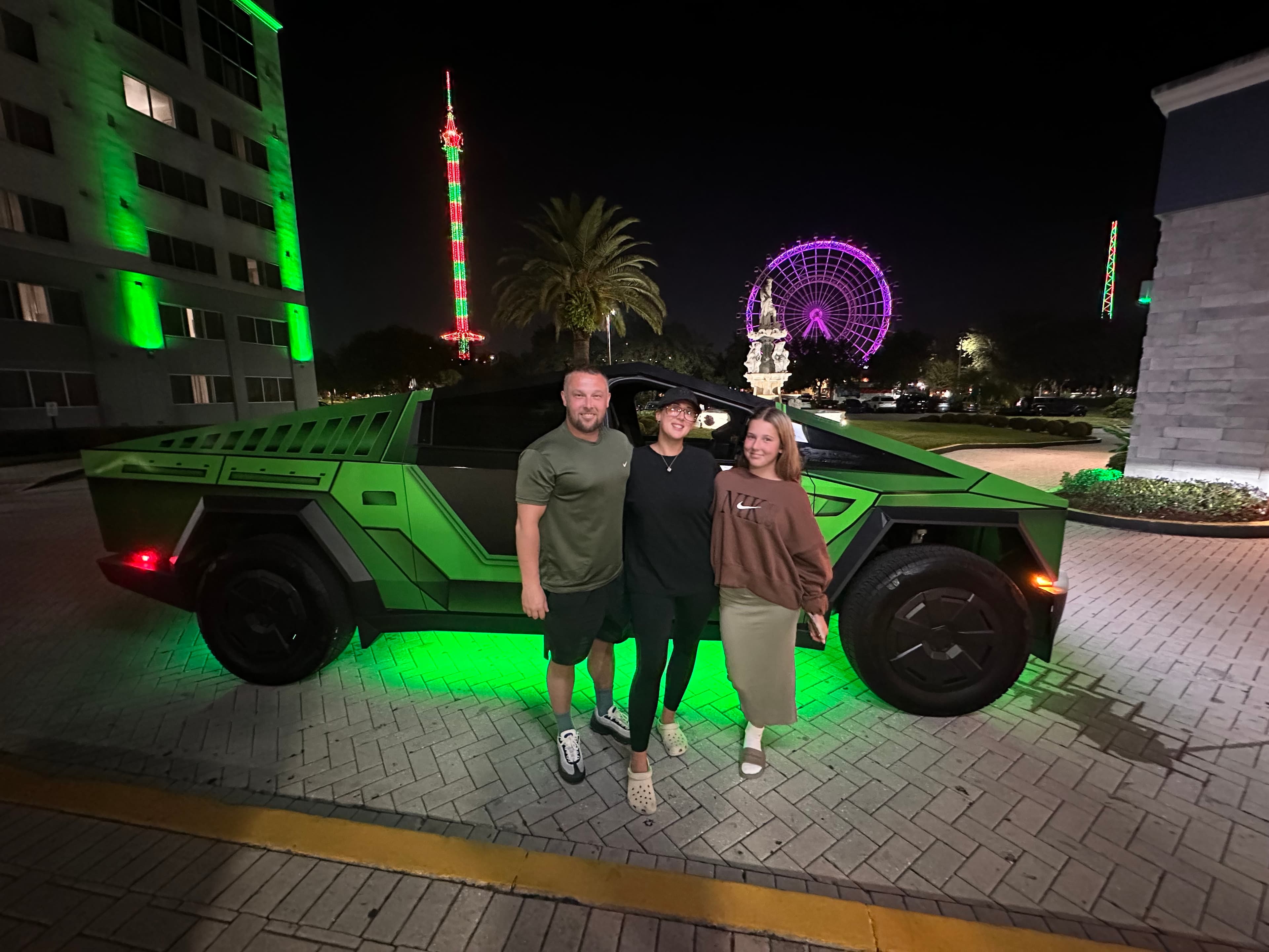 Family with green-lit Cybertruck on International Drive at night