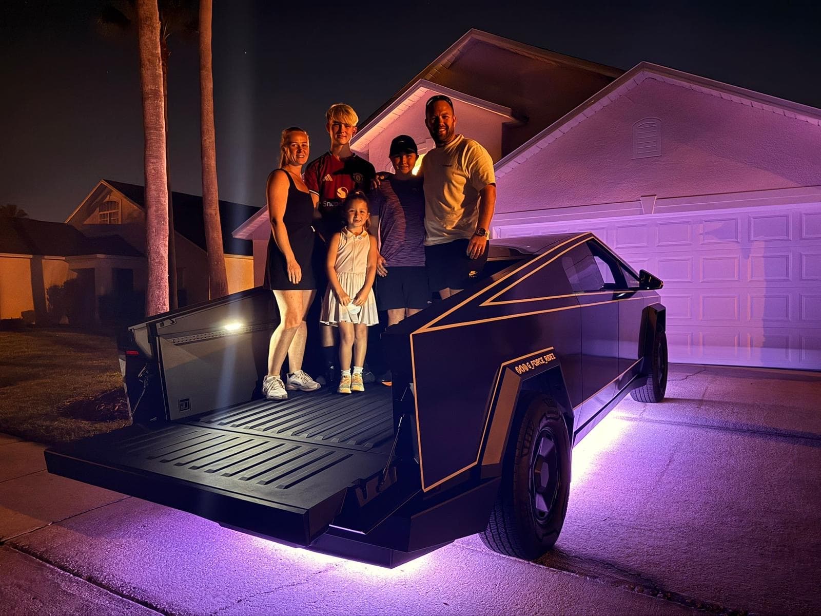 Family posing on the Cybertruck bed at night with purple underglow